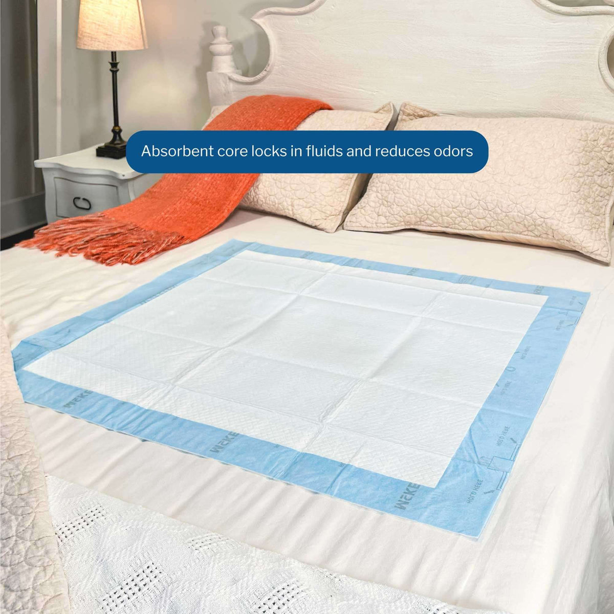 Disposable underpad with white absorbent top and blue backing laid flat on a white bed in a bedroom setting