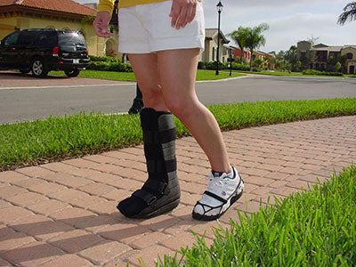 Shoe leveler worn on sneaker beside walking boot, showing even height balance while person walks on brick path outdoors