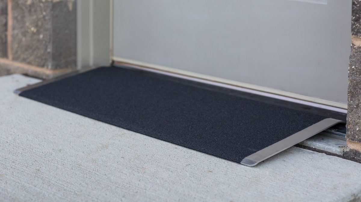 Threshold ramp with black textured non-slip surface and aluminum edges, installed at a doorway over a concrete step
