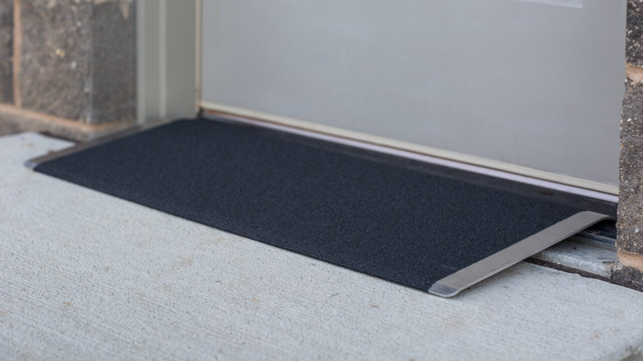 Threshold ramp with black textured non-slip surface and aluminum edges, installed at a doorway over a concrete step