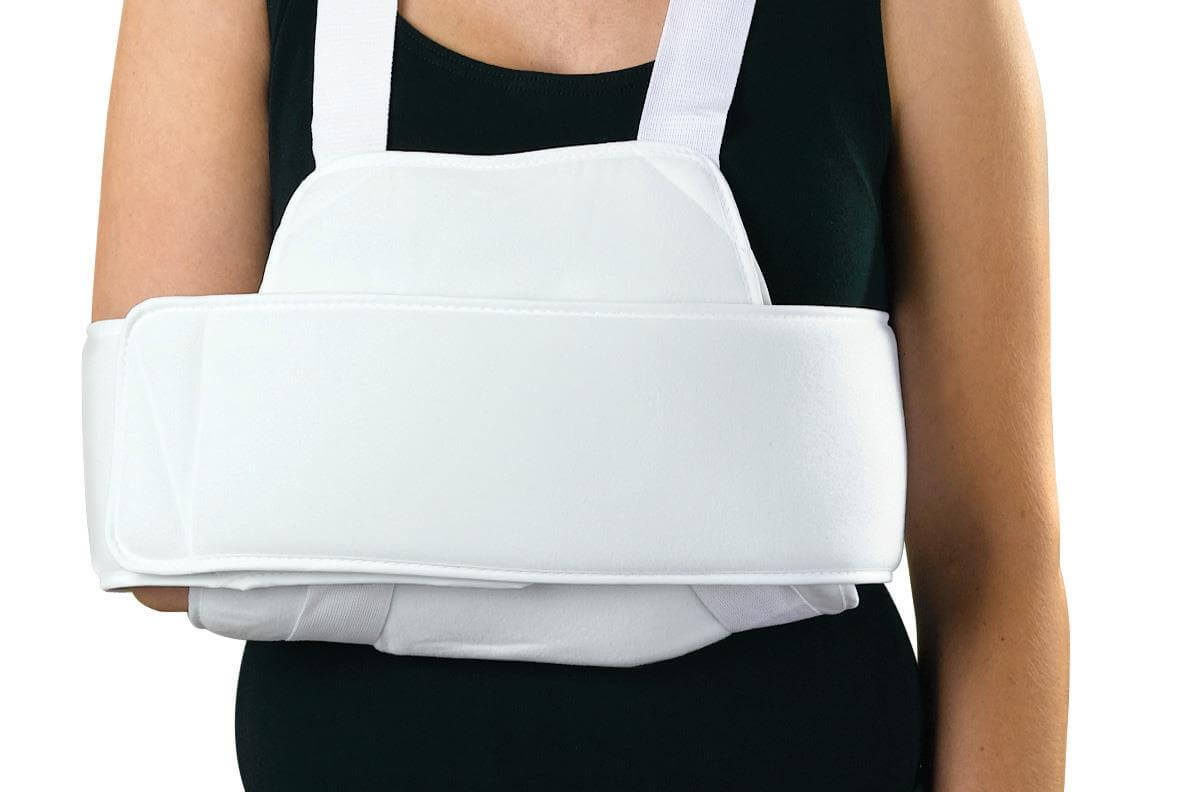 Sling and swathe shoulder immobilizer in white worn by a person over a black sleeveless top, securing the arm against the