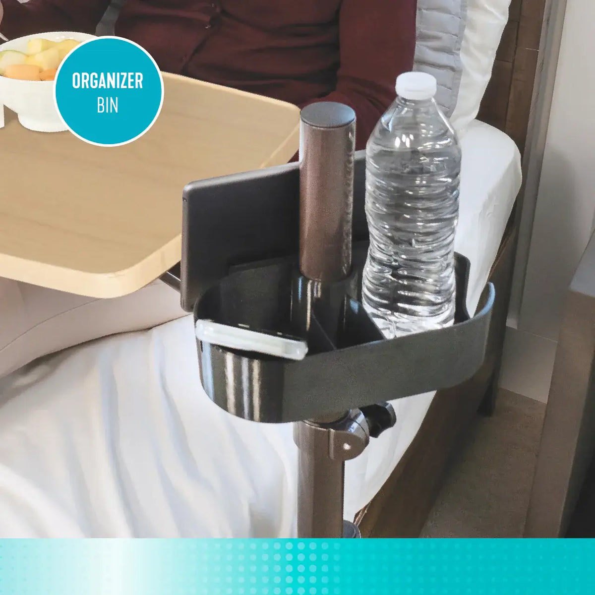 Over bed table organizer bin attachment holding a water bottle and personal items, mounted on a pole beside a hospital-style