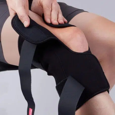 Knee brace being fastened around a bent knee, black neoprene wrap style with adjustable straps and open patella design