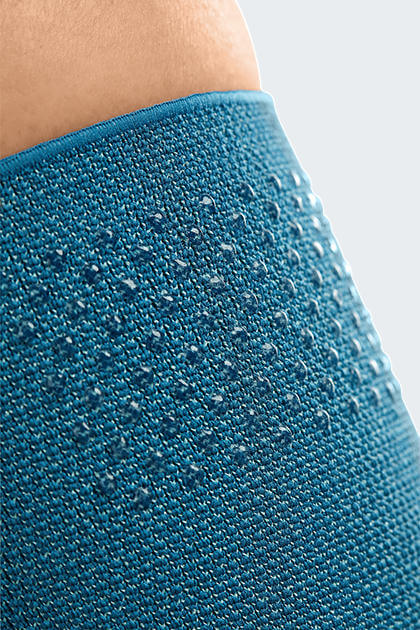 Knee support close-up showing teal knit fabric texture with silicone dot grip pattern and finished top band worn on leg
