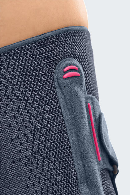 Knee support with gray knitted fabric worn on leg, featuring pink silicone ribbed patellar pad and side stabilizer panel