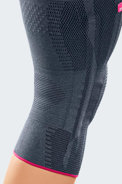 Genumedi knee support in gray knit fabric with pink trim, worn on leg, showing textured compression zones around kneecap