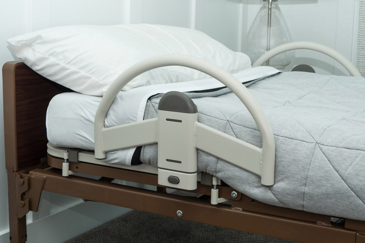 Bed handle with arched grab bar and center support bracket mounted to a brown-framed hospital bed with white bedding
