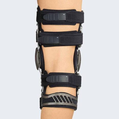 Hinged knee brace with black straps, bilateral metal uprights, and dial hinges worn on a leg, side view