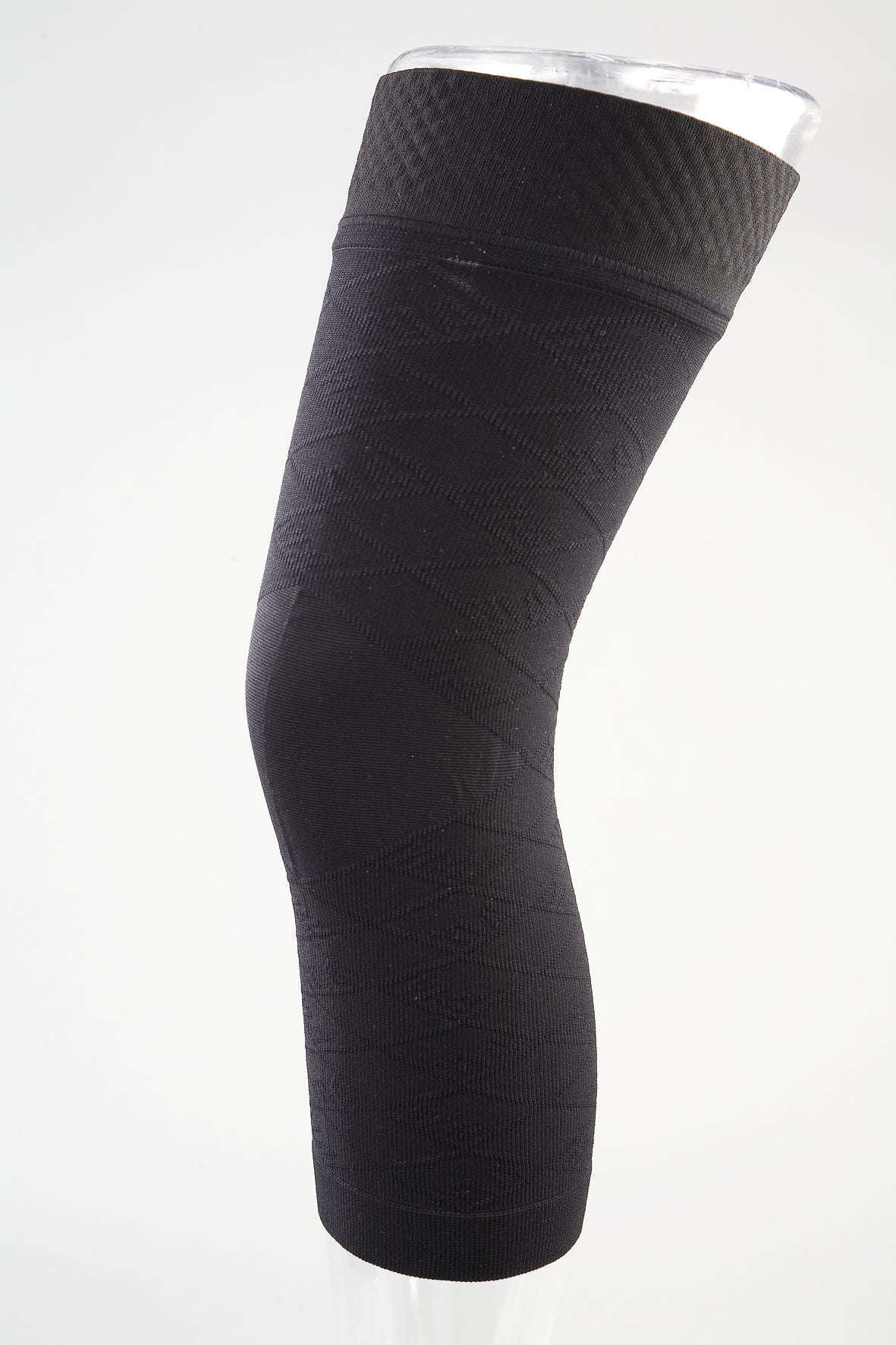 Knee brace undersleeve in black seamless knit fabric displayed on a clear leg form, side view