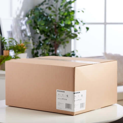 Disposable underpad product in a sealed McKesson branded cardboard shipping box on a white surface with plants in background