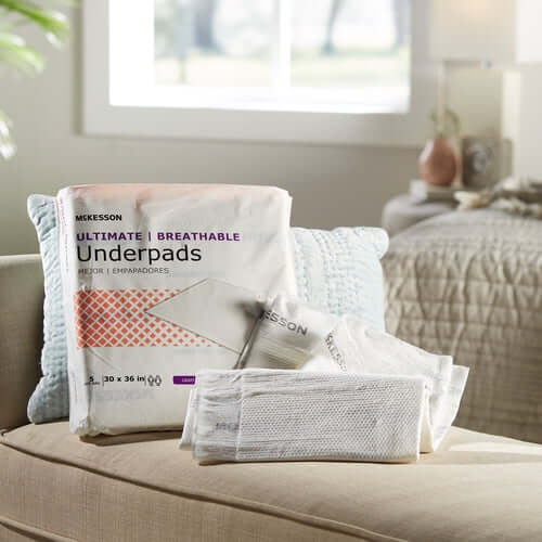 Disposable underpads package and individual pads displayed on a beige sofa in a home setting