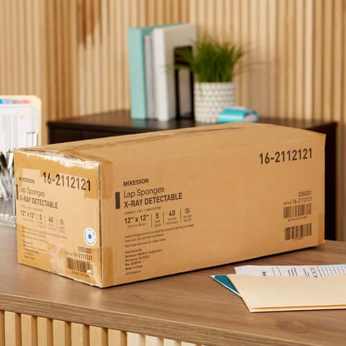Boxed McKesson x-ray detectable lap sponges, 12x12 inch, 5 count per pack, 40 packs per case, on a wooden desk
