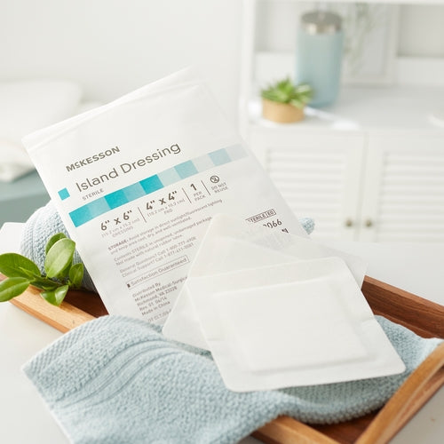 McKesson Island Dressing sterile square wound dressing shown in packaging alongside two unwrapped dressings on a wooden tray