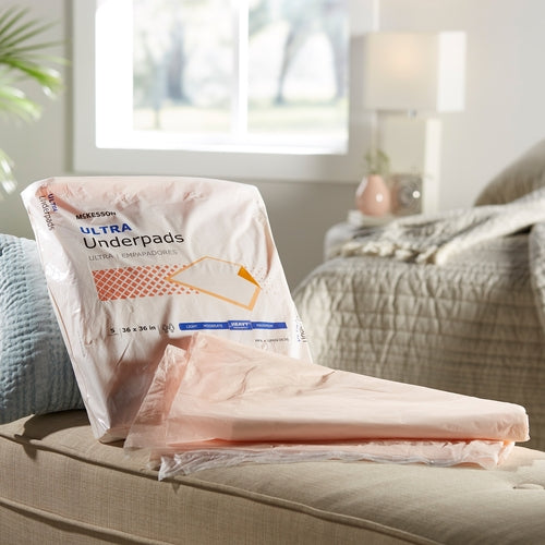 Disposable underpads in open McKesson Ultra packaging resting on a couch in a bedroom setting