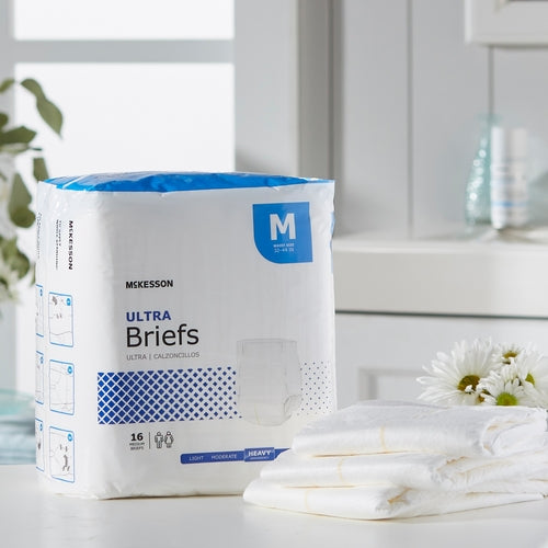 McKesson Ultra Briefs incontinence brief package in medium size, displayed next to folded white briefs and white flowers