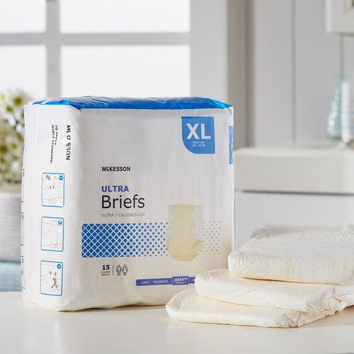 McKesson Ultra Briefs XL package of 15 adult incontinence briefs beside two unfolded white briefs on a white surface