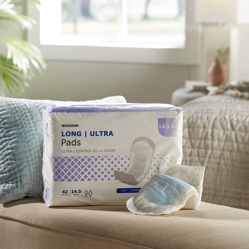 Bladder control pad package labeled Long Ultra beside a single unwrapped pad on a couch in a bright bedroom setting