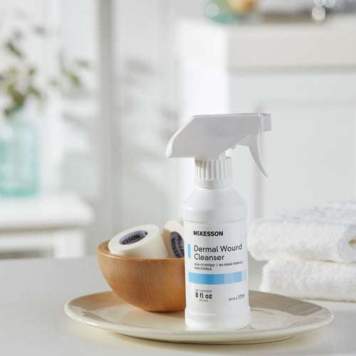 McKesson Dermal Wound Cleanser 8 oz spray bottle on a plate with medical tape rolls and folded towels nearby