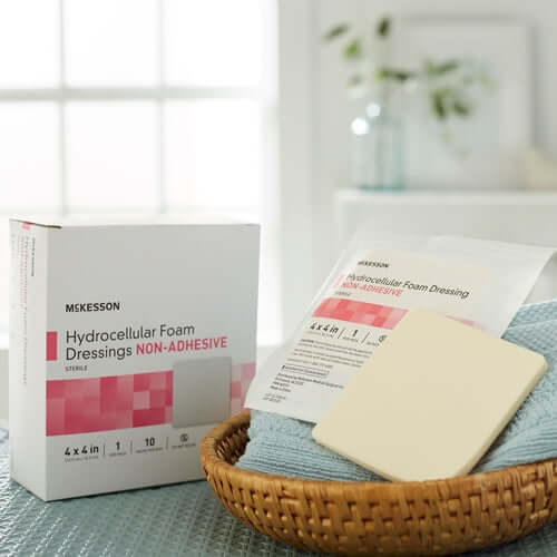 McKesson hydrocellular foam dressing box beside an open package with a square foam pad in a wicker basket on a teal towel