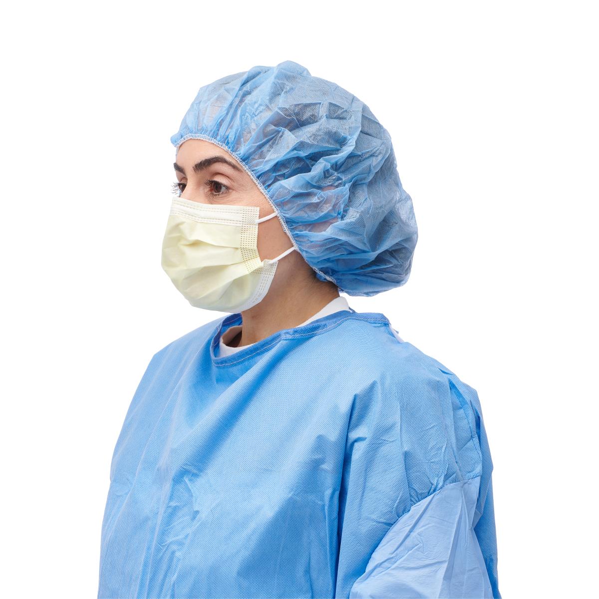Isolation face mask with earloops in yellow worn by person in blue surgical gown and bouffant cap, side view on white