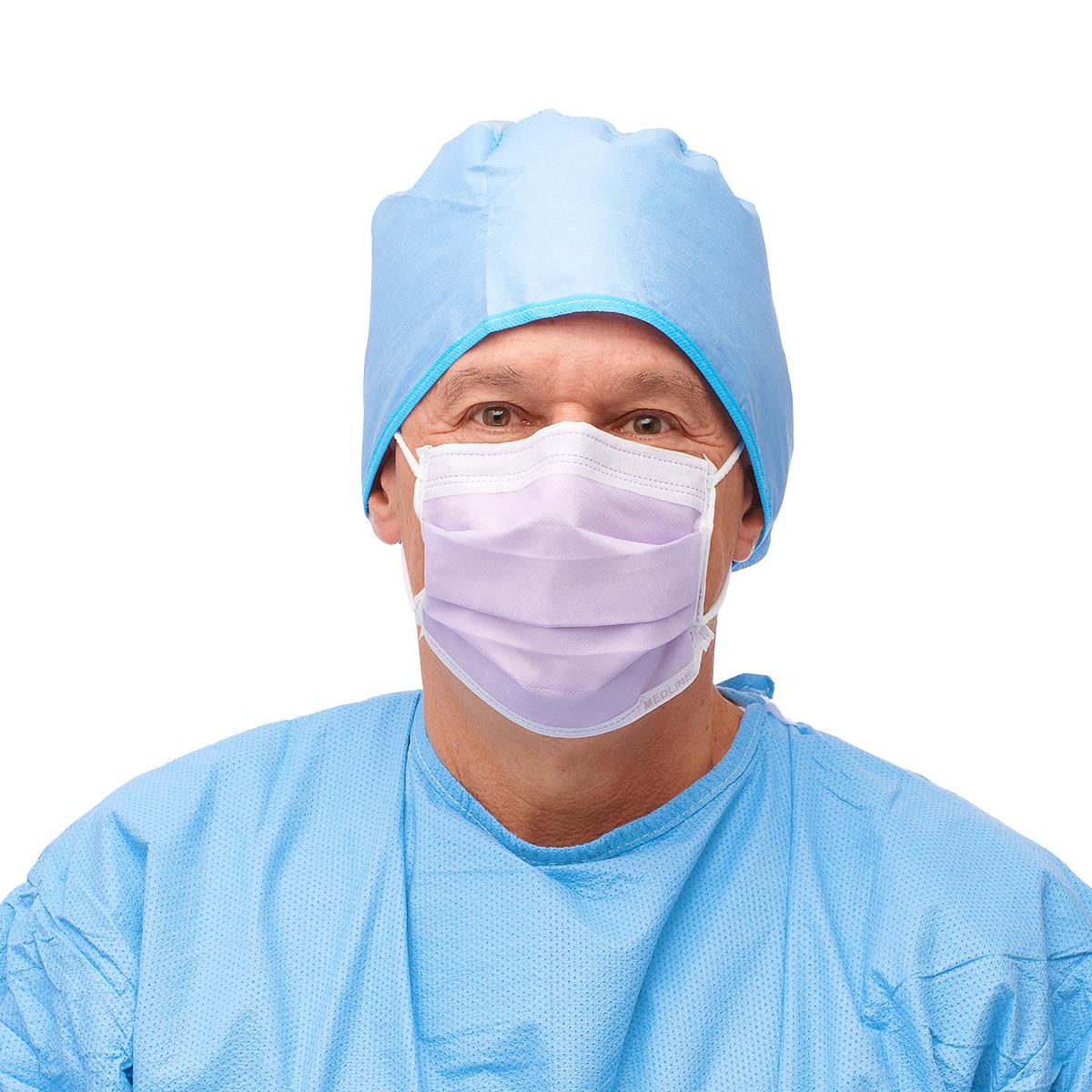 Disposable procedure face mask in lavender with ear loops, worn by a person in blue surgical scrubs and cap