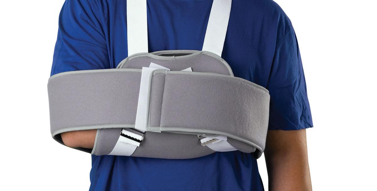 Shoulder sling and swathe immobilizer worn on person in blue shirt, gray padded design with white straps securing arm to body