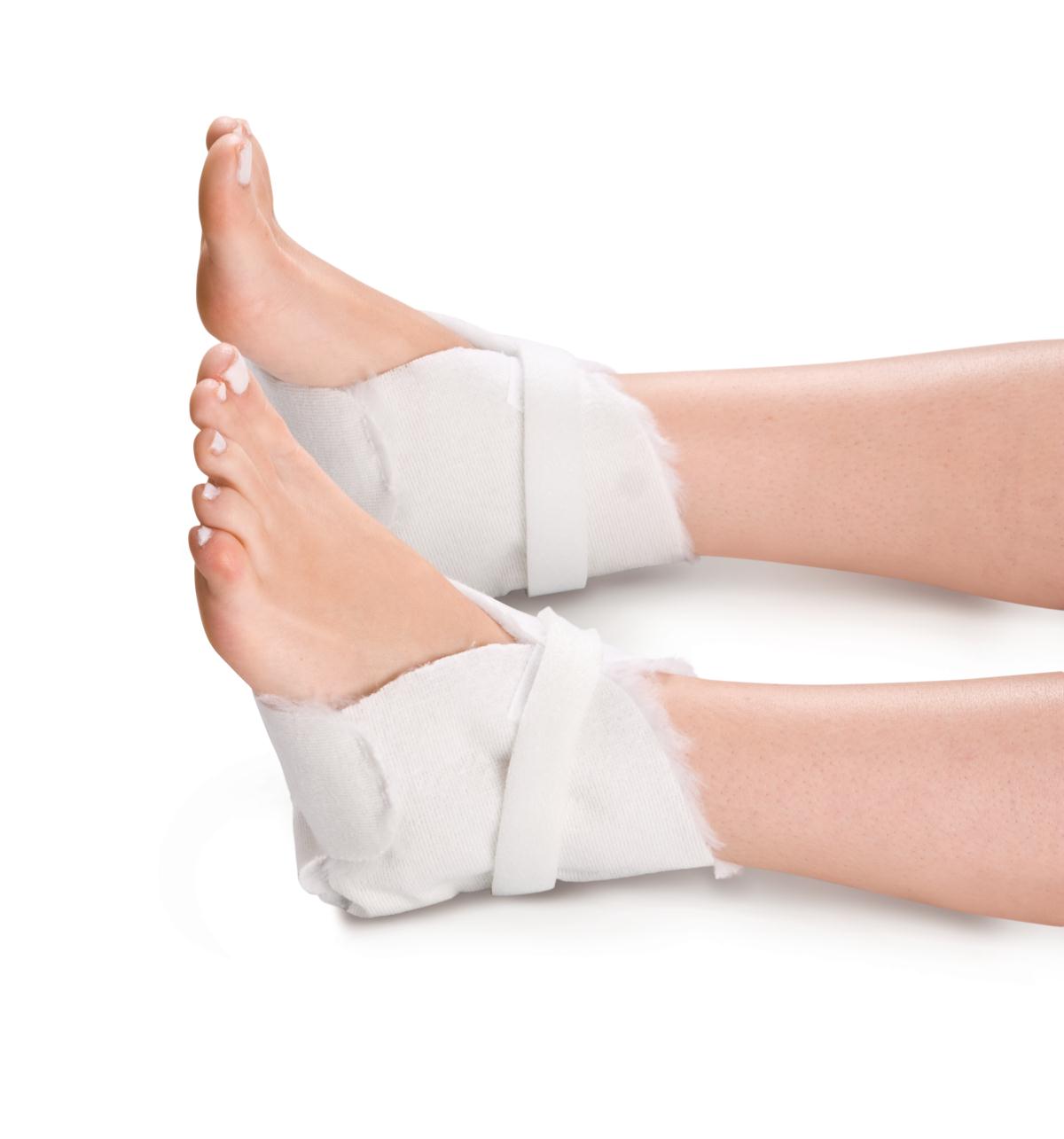 Economy heel protectors in white fleece-lined wrap style worn on both heels, secured with hook-and-loop straps