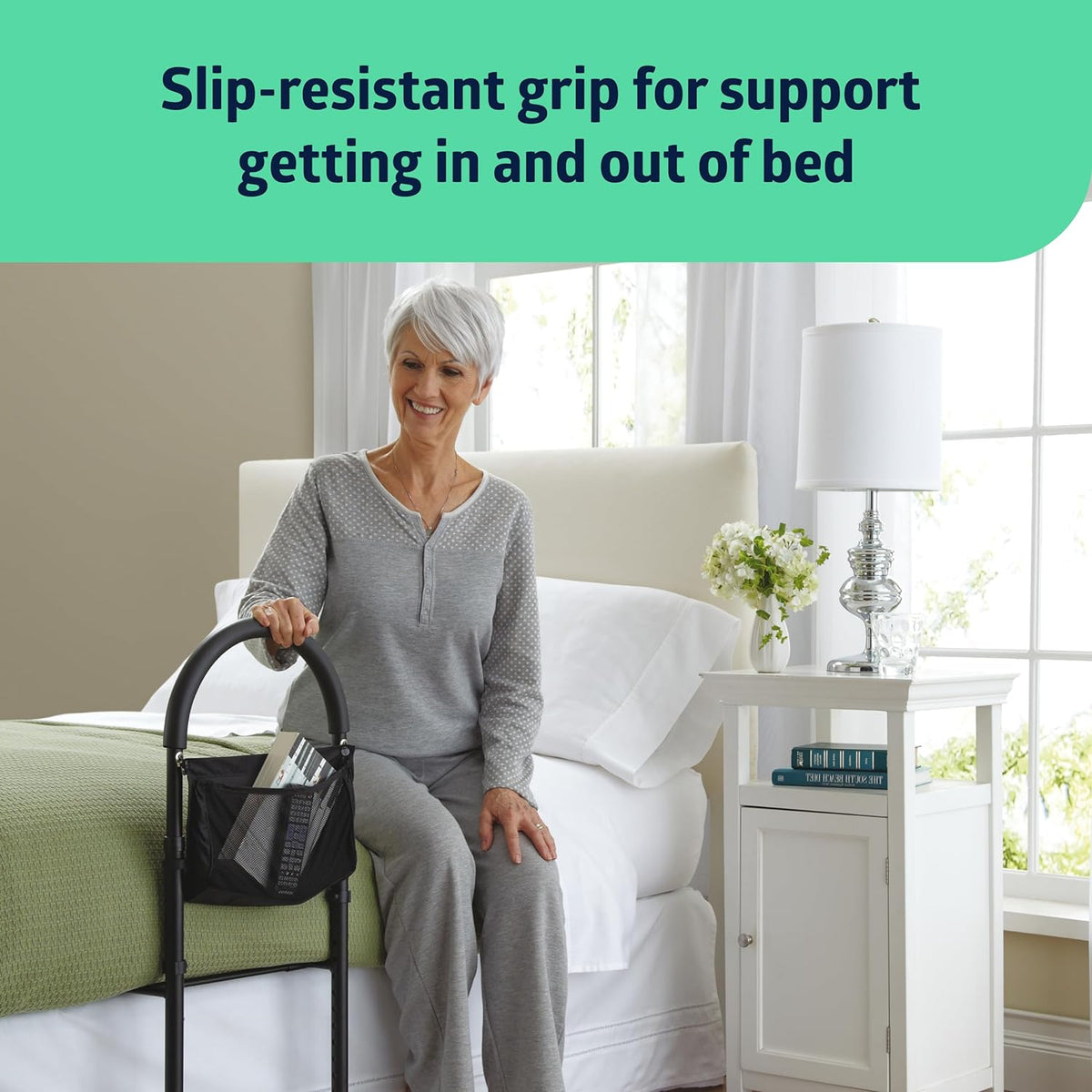 Bed assist bar with storage pouch beside a bed, gripped by a smiling older woman seated on the edge of a white bed