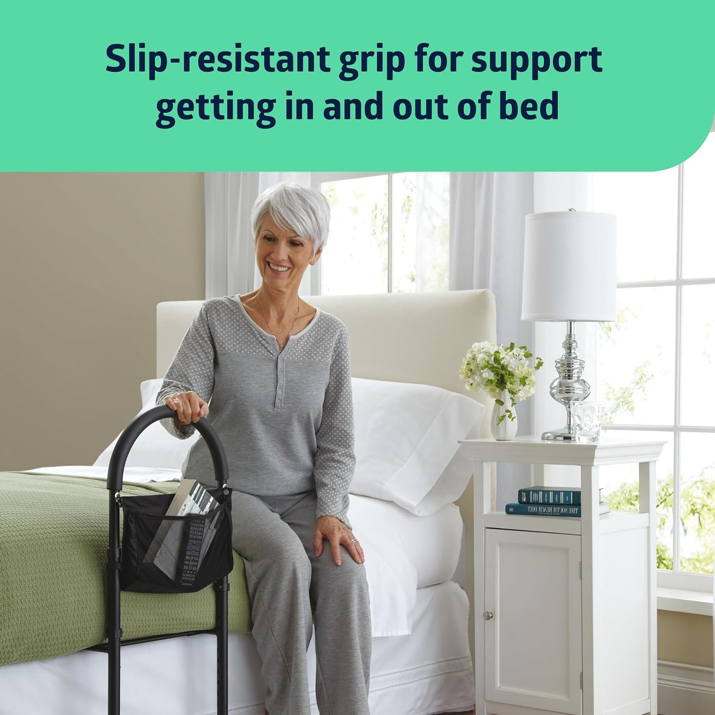Bed assist bar with storage pouch beside a bed, gripped by a smiling older woman seated on the edge of a white bed
