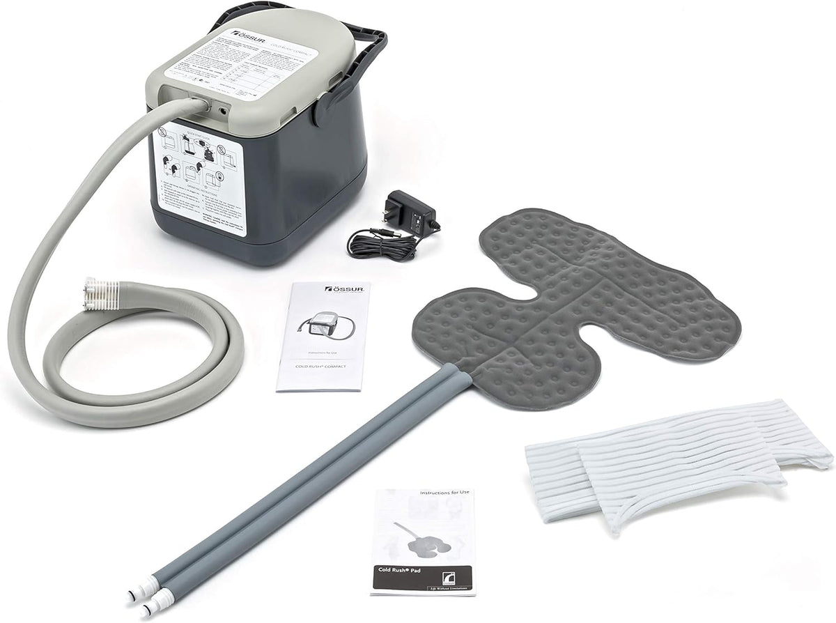 Ossur Cold Rush Compact cold therapy machine with tubing, shoulder pad, straps, power adapter, and instruction manuals laid