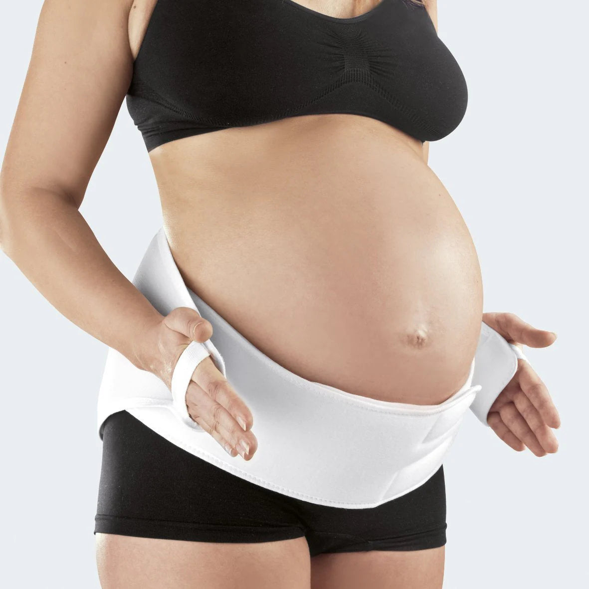 Maternity support belt in white worn low on the abdomen of a pregnant woman in black athletic wear