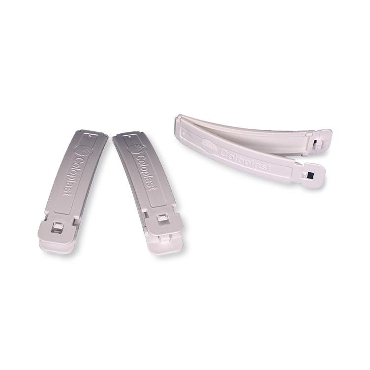 Drainable pouch clamps by Coloplast shown closed and open, white plastic with locking mechanism, set of two