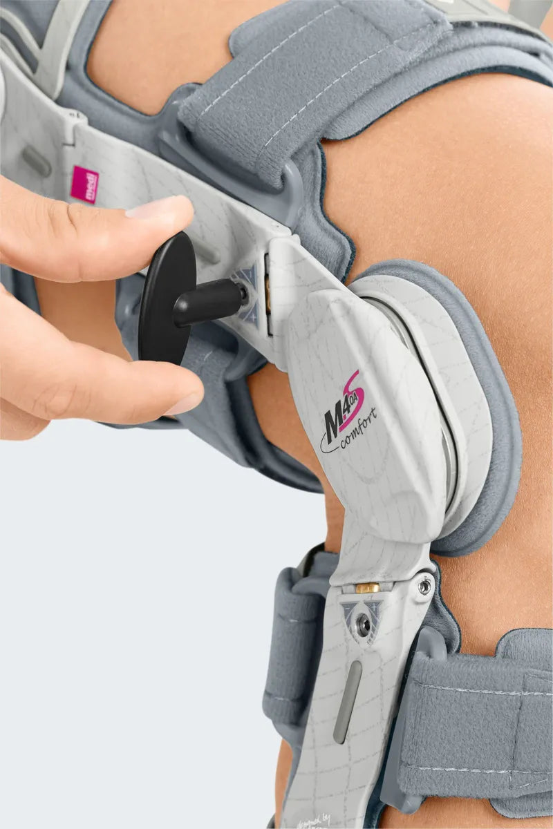 Knee brace with hinged joint mechanism worn on leg, hand adjusting the lateral dial on the M.4s OA Comfort brace