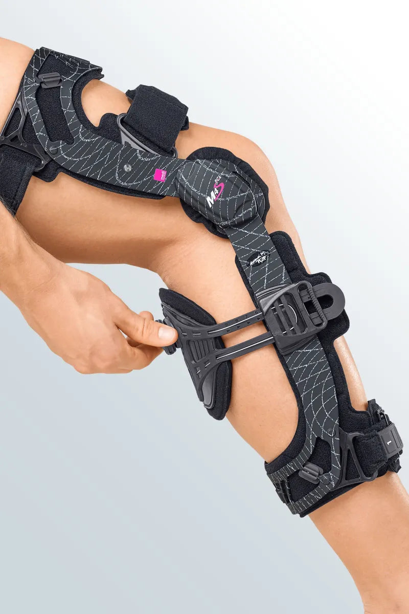 Knee brace with dark patterned fabric, rigid side uprights, hinged joint, and adjustable straps worn on a bent leg