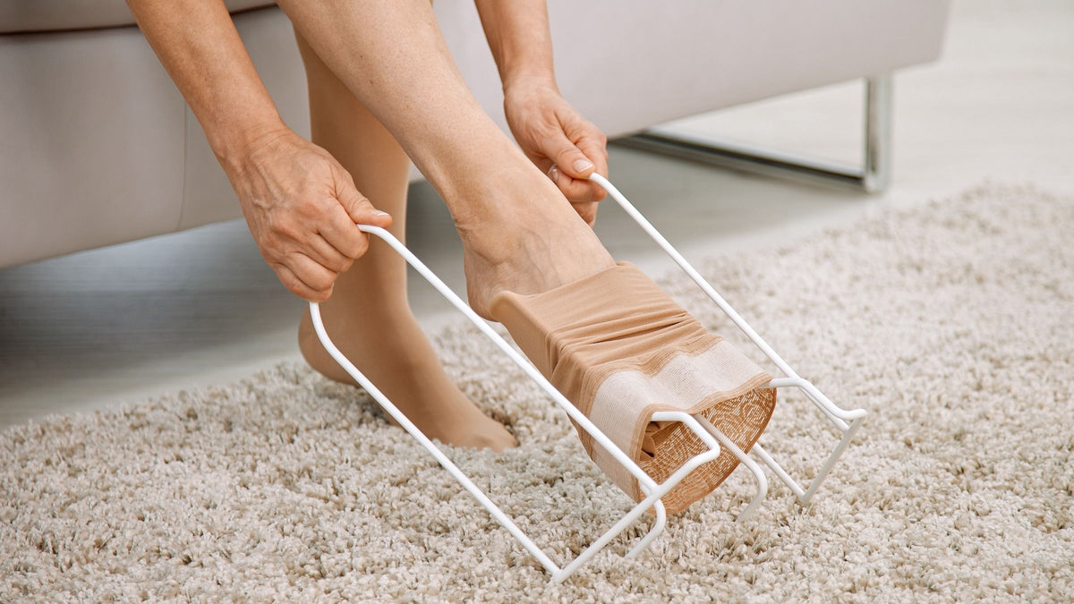 Compression stocking donning aid being used to slide a beige compression sock onto a foot over a carpeted floor