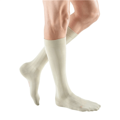 Compression socks in cream worn on a man's lower legs, knee-high length with ribbed texture and closed toe