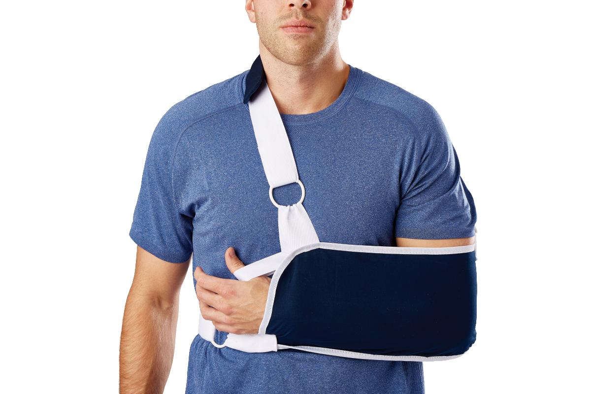 Shoulder immobilizer sling in navy and white worn by a man over a blue t-shirt, supporting the forearm and arm close to the