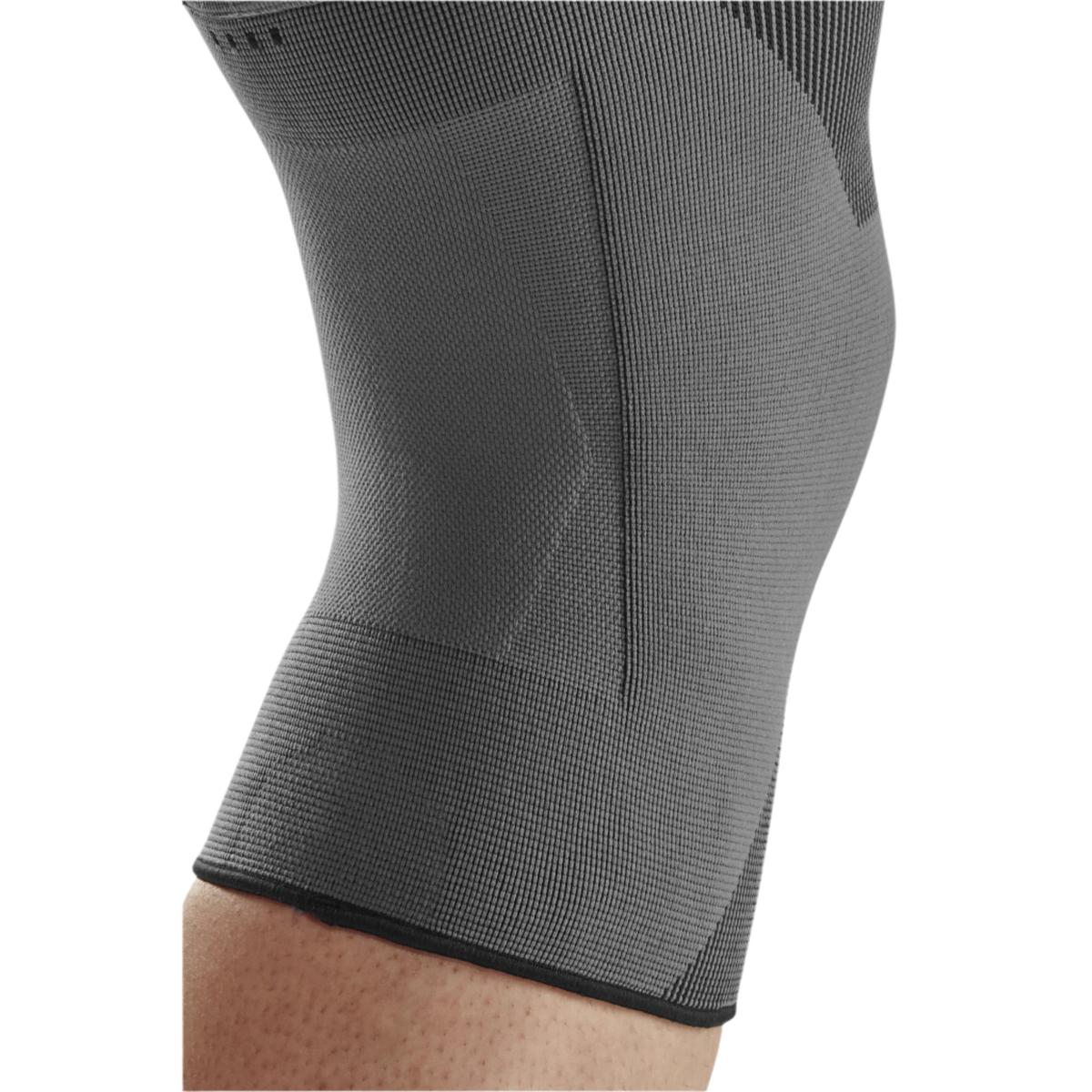 Knee sleeve in gray knit fabric worn on a leg, showing close-up of textured compression fabric and lower hem