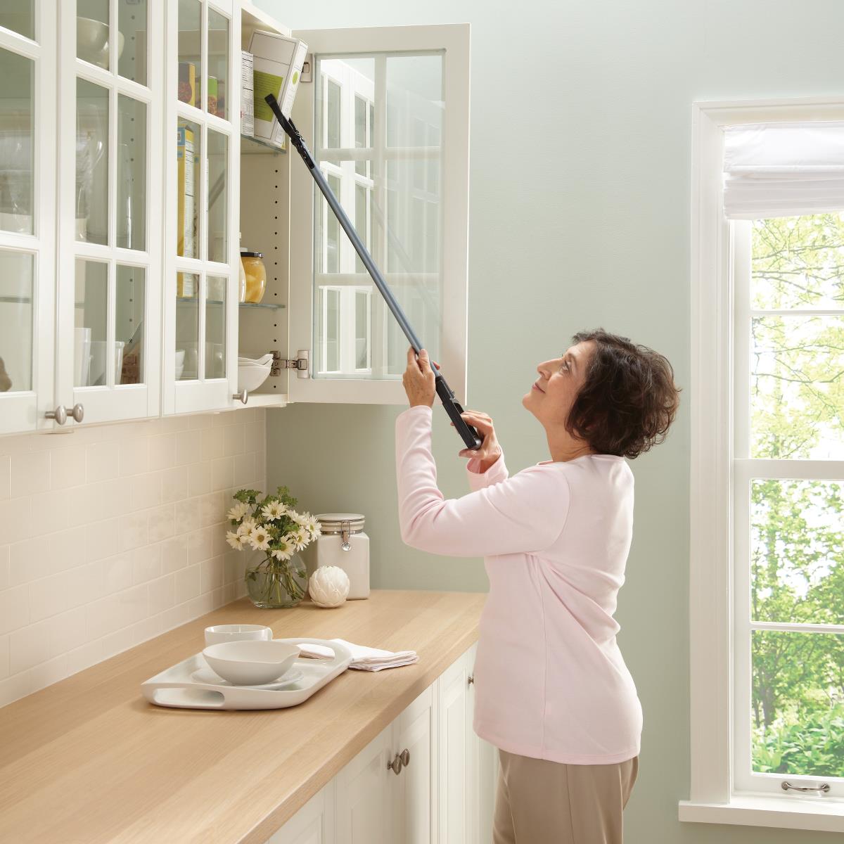 Reacher tool with padded grip used by a woman to access items in a high kitchen cabinet