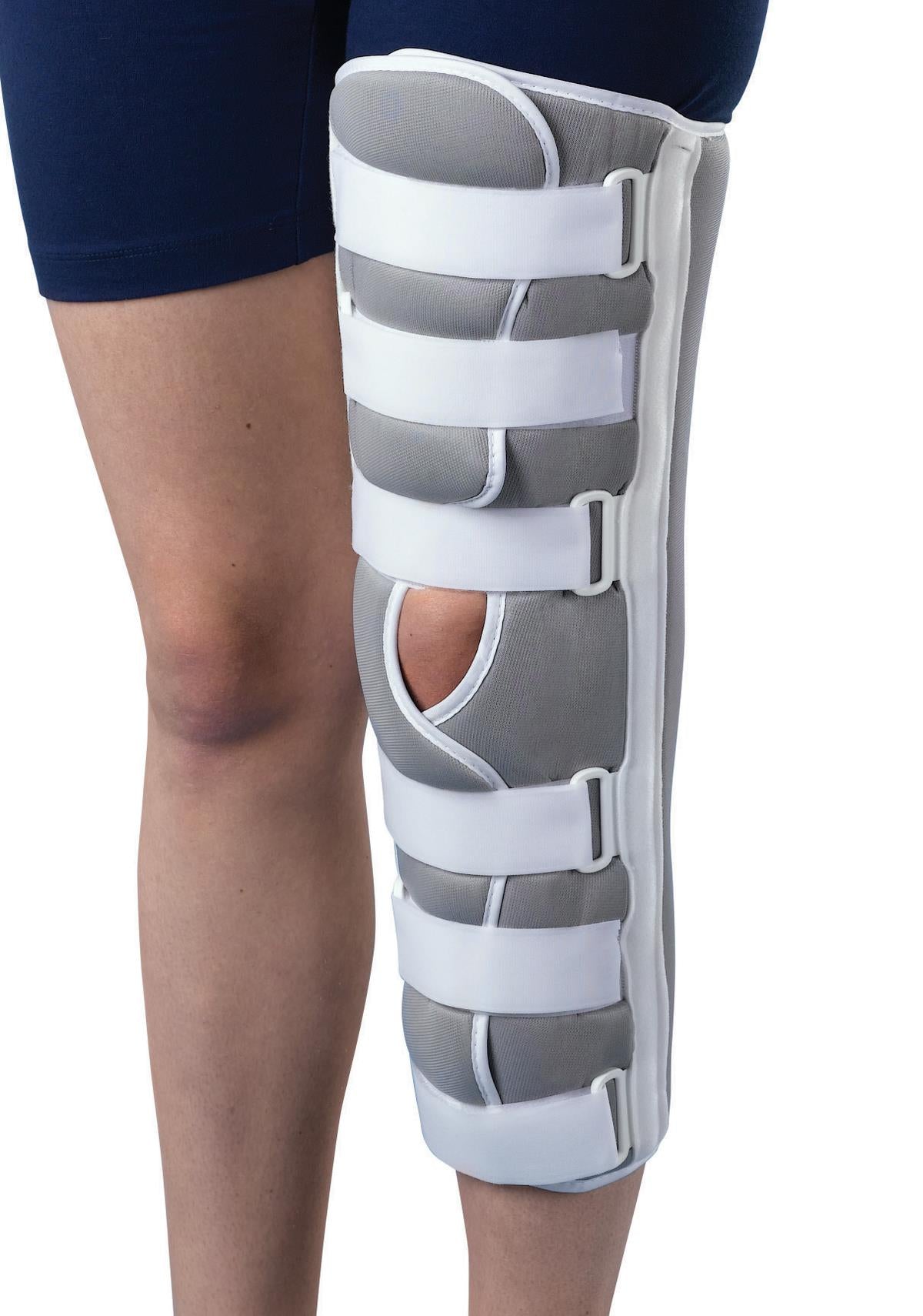 Knee immobilizer in white and gray tricot foam with open patella cutout and four adjustable hook-and-loop straps, worn on
