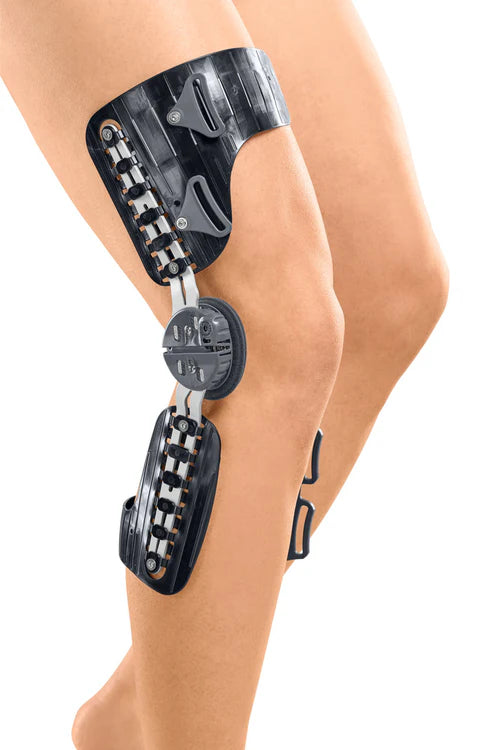 Knee brace with hinged carbon frame, adjustable dial joint, and padded cuffs worn on a bare leg, side view