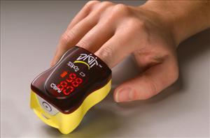 Digit finger pulse oximeter clipped onto a finger displaying red LED readout on dark brown and yellow device