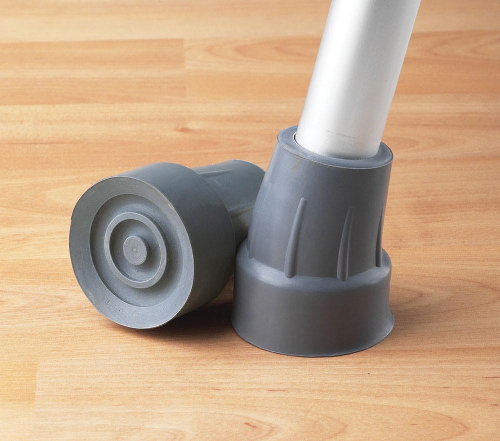 Crutch tip replacement rubber caps in gray, one fitted on a crutch leg and one lying flat on a wood floor