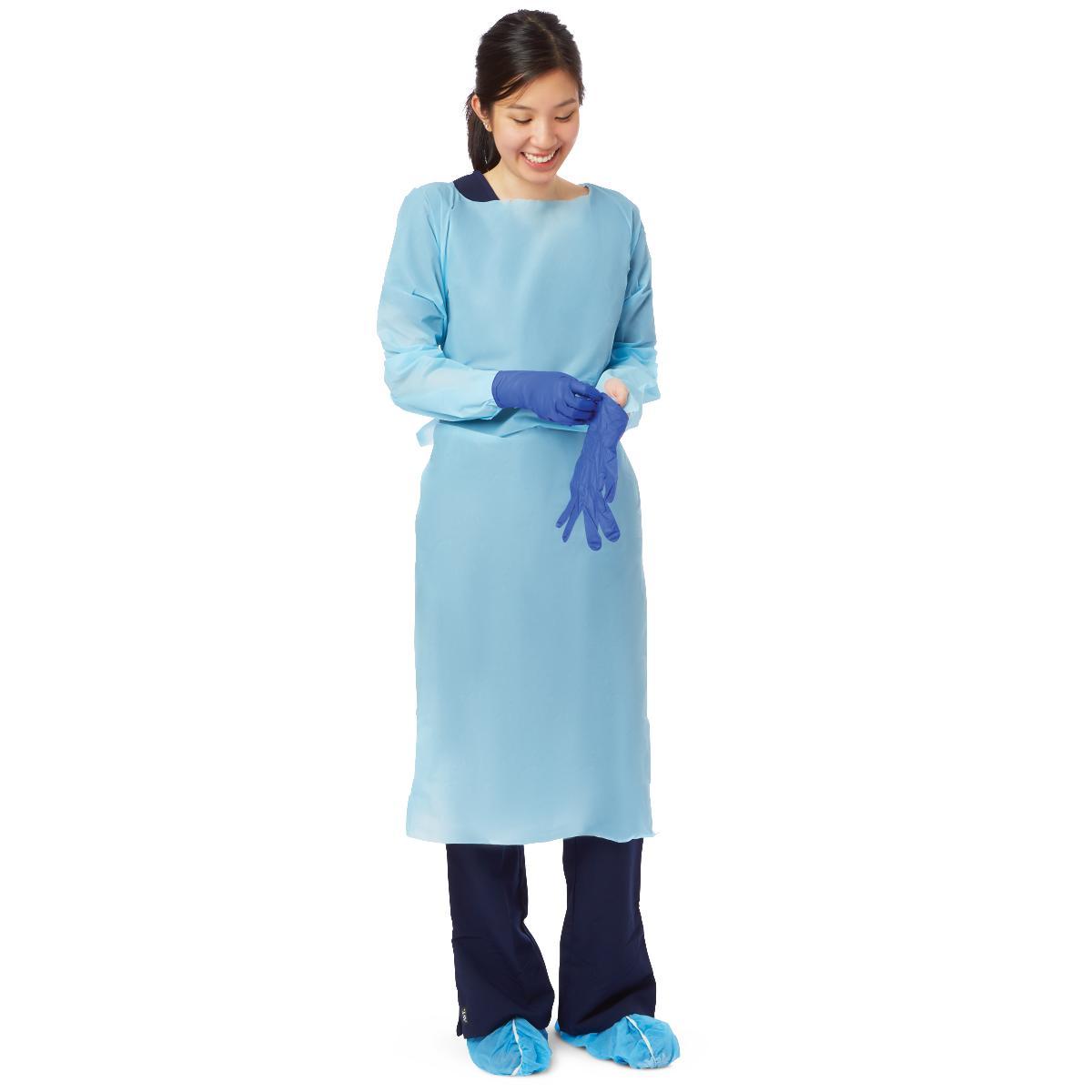 Disposable isolation gown in light blue worn by a smiling woman pulling on blue nitrile gloves with shoe covers