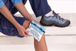 Cold pack being applied to a person's knee while seated on steps, wearing athletic shorts and sneakers