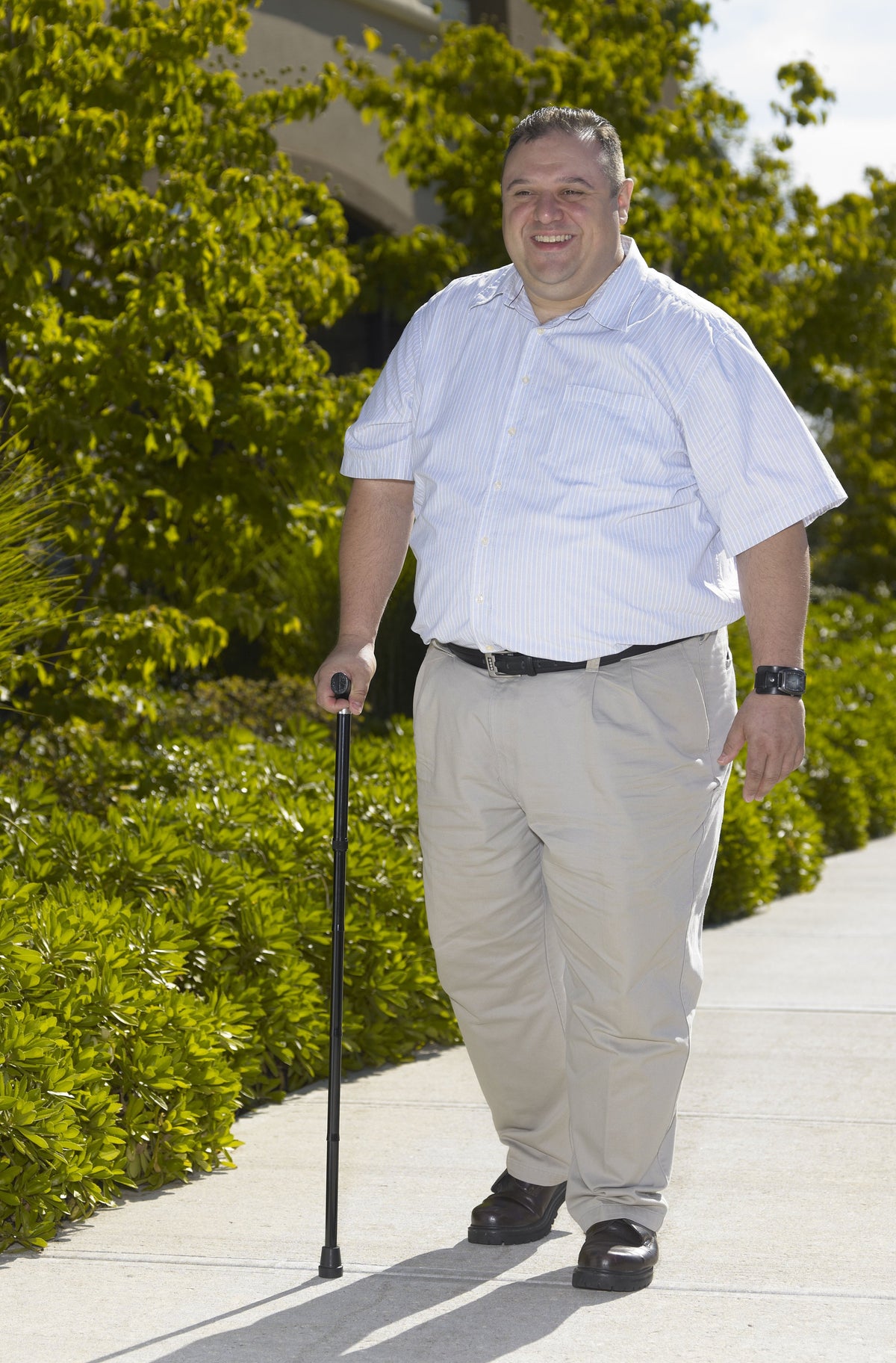 Heavy duty folding cane with T-handle used by a smiling man walking outdoors on a sunny sidewalk