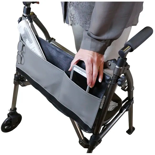 Walker bag accessory shown open on a folding walker, with a person placing a smartphone inside alongside glasses and papers