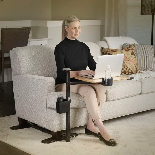 Swivel tray table with wooden surface and cup holder beside a chair, with woman using a laptop while seated in living room