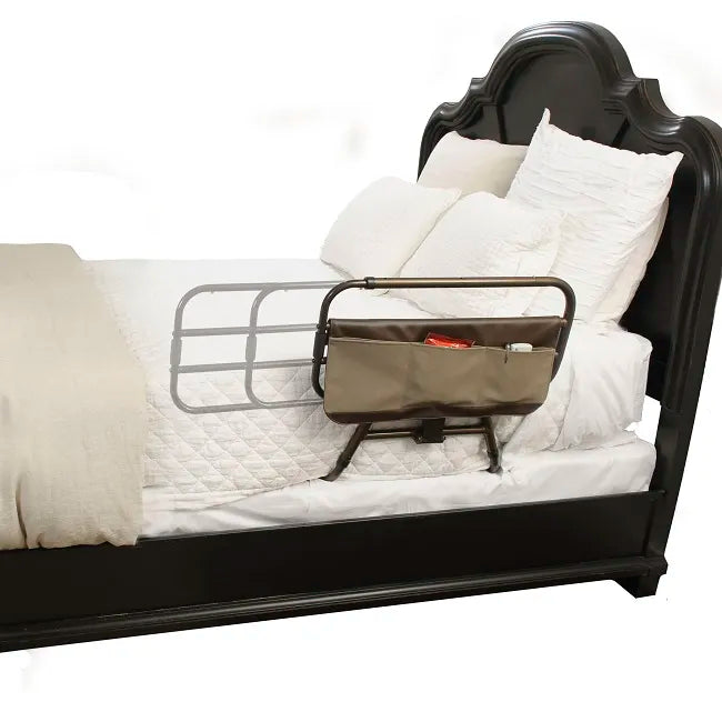 Bed rail with attached tan fabric organizer pocket installed on the side of a dark wood home bed with white bedding