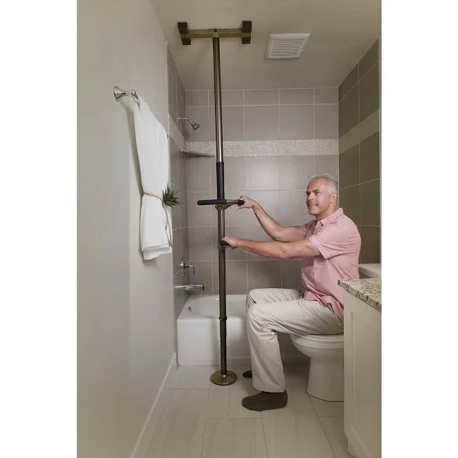 Floor-to-ceiling tension safety pole with two grab handles, shown in use by a man seated on a toilet in a tiled bathroom